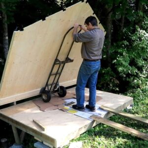 A shed like a plywood box, overhanging a slope.